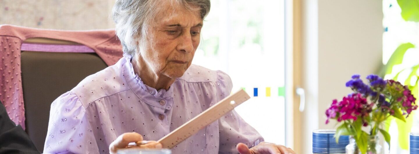 Das Bild zeigt eine älter Frau, die ein Lineal in der Hand hält.